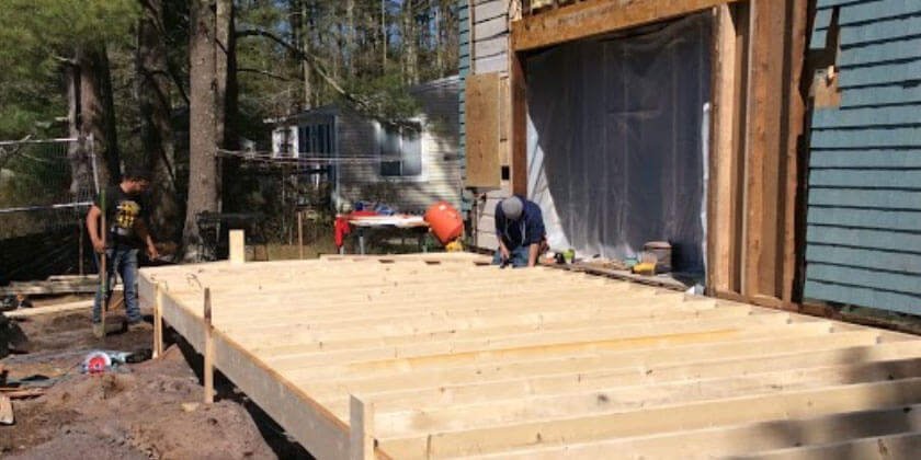 Deck builders in Malden, CA, construct a wooden deck next to a blue house.