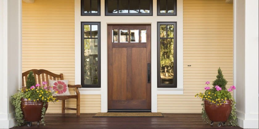 A welcoming front porch with a wooden door flanked by windows, a bench, and potted flowers, meticulously crafted by a Boston-based general contractor.