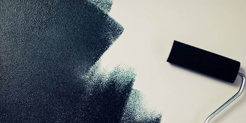 A contractor applying dark paint to a white surface with a paint roller, creating a textured pattern.