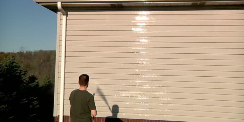 A general contractor pressure washing the siding of a house, with the cleaned area visibly brighter.
