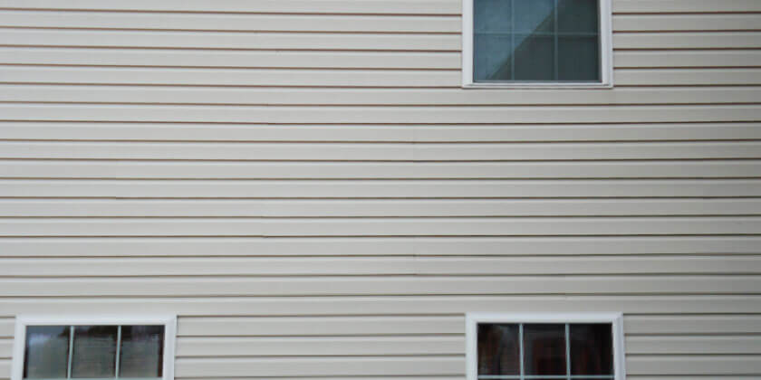 Exterior wall of a building, completed by a general contractor, with horizontal vinyl siding and two windows.